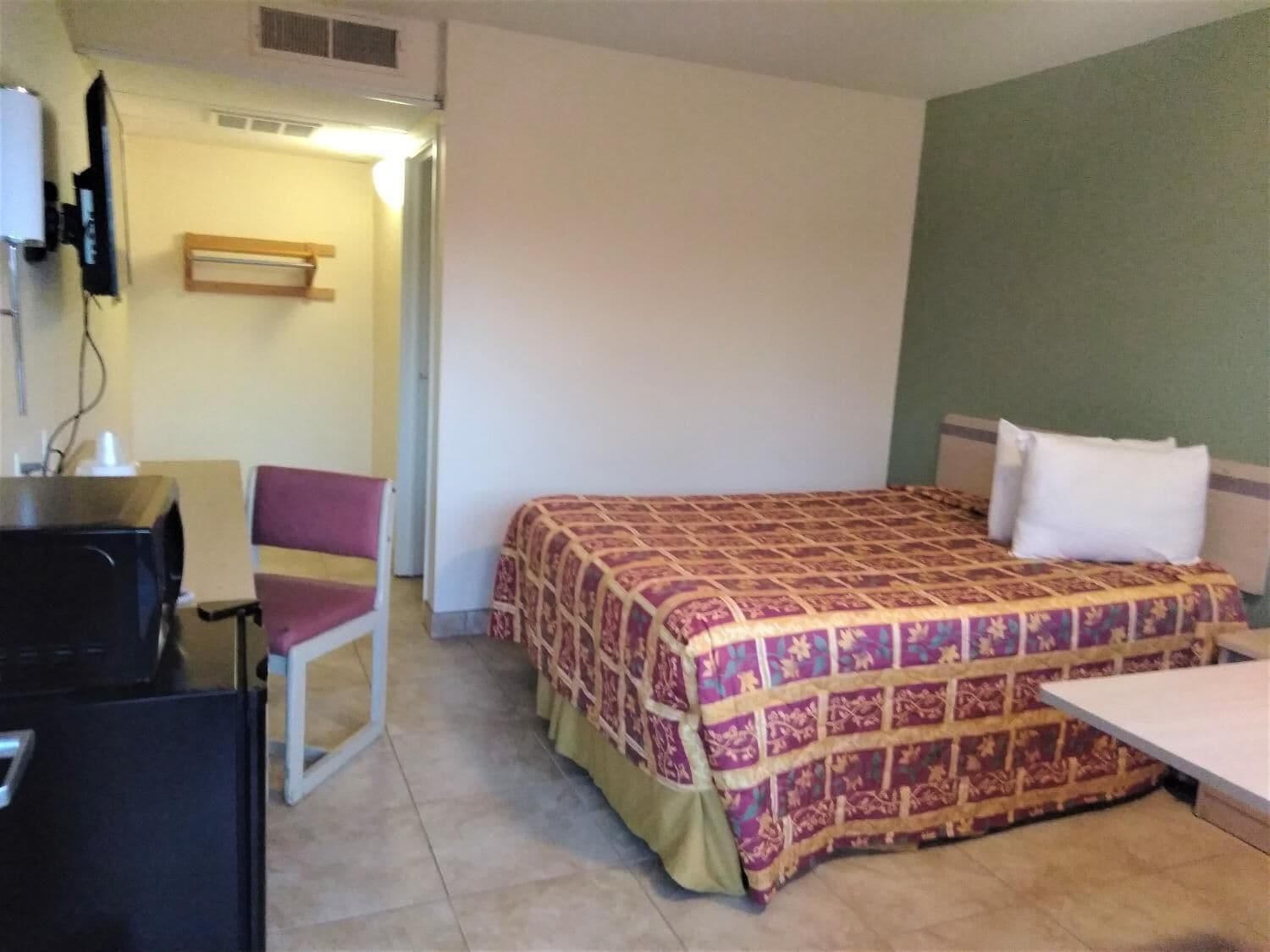 A small hotel room with a bed, a desk, and a chair.
