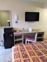 Habitación de hotel con cama, escritorio con silla, televisor montado en la pared, refrigerador y basurero.