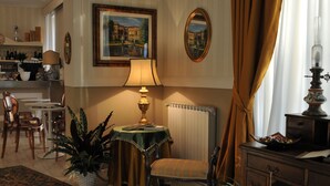 A well-furnished living room with a table, chairs, a lamp, a potted plant, a mirror, and a painting on the wall. - Hotel Stipino (Lucca)