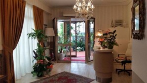 A hotel lobby with a chandelier, a reception desk, a chair, and potted plants. - Hotel Stipino (Lucca)