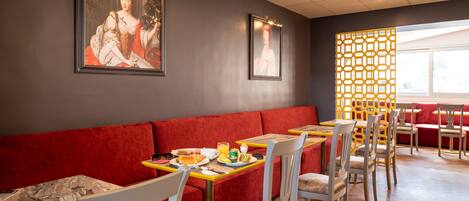 A restaurant with red seating, tables with yellow and white chairs, and framed artwork on the walls.