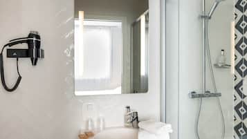 Een badkamer met een witte wastafel, een spiegel, een haardroger, een douche en een fles shampoo.