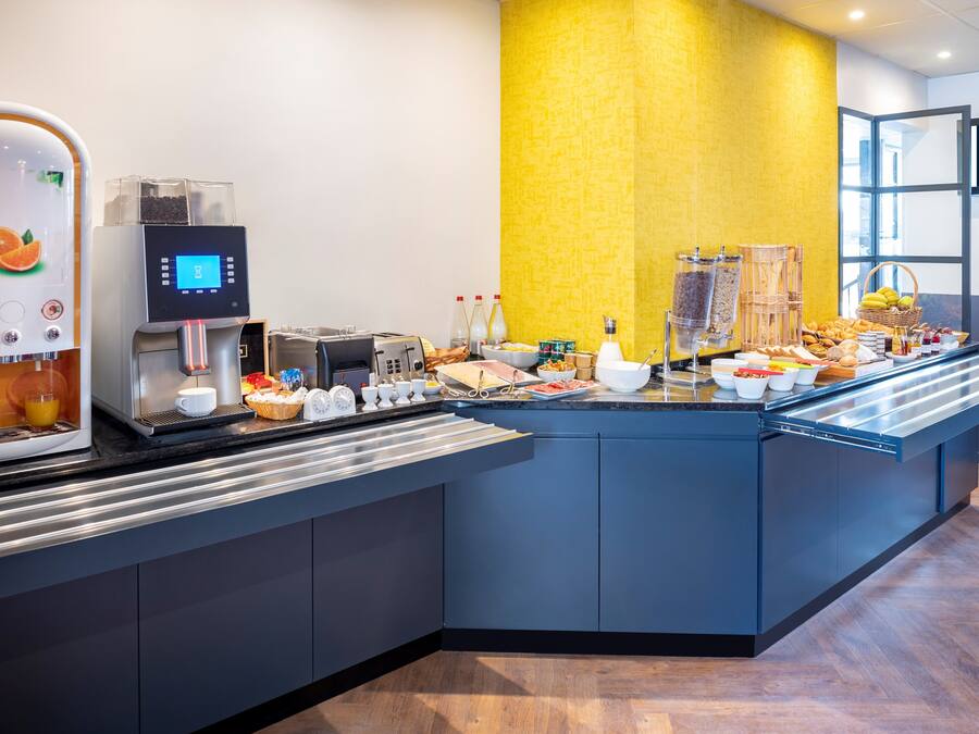 Un bufé de desayuno de hotel con una máquina de café, una estación de té y diversas opciones de comida.