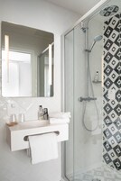 A modern bathroom with a glass-enclosed shower, a white vanity with a mirror, and a patterned wall.