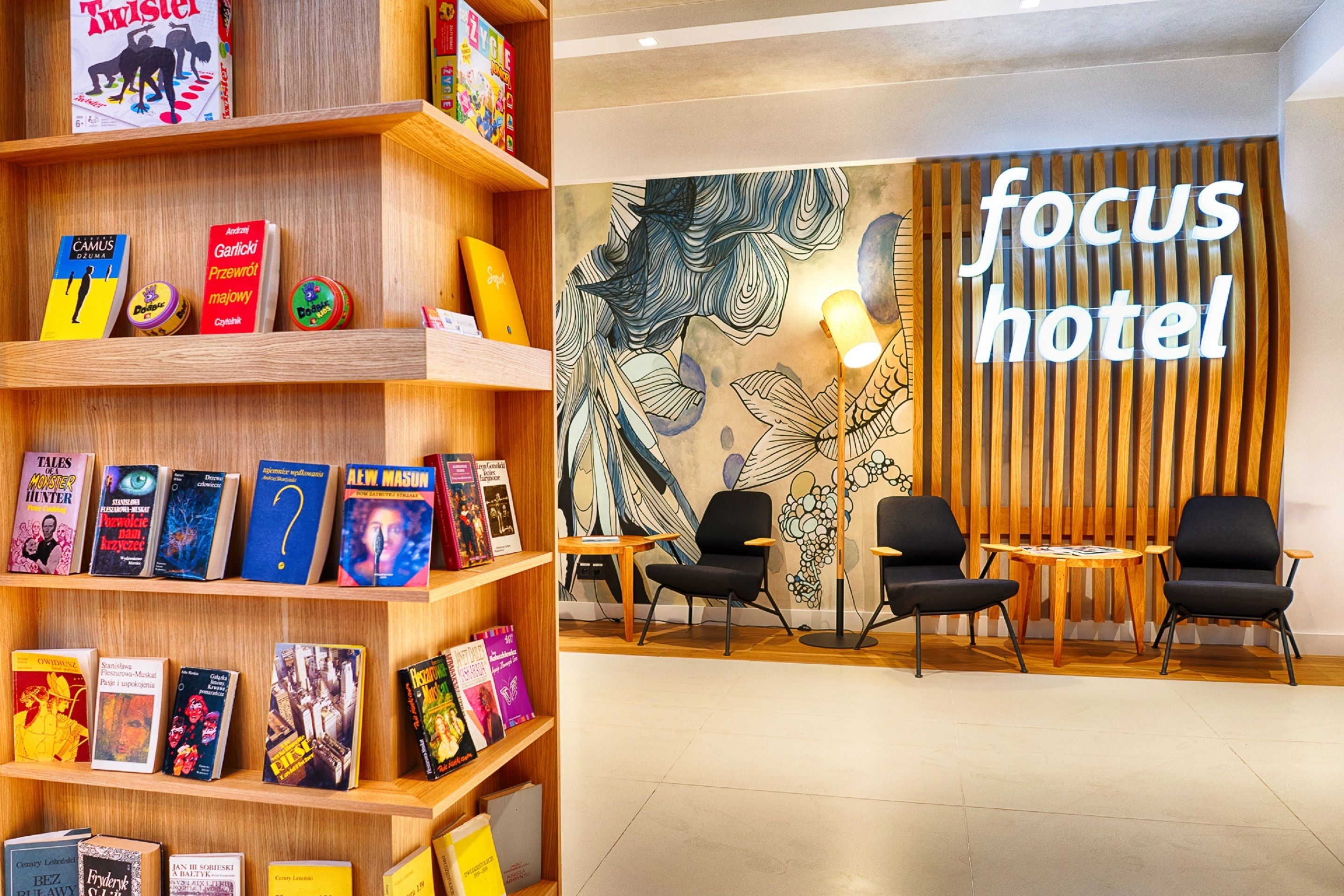 Een hotel lobby met houten schappen vol boeken, een muurschildering en een bord met de tekst 'focus hotel'.