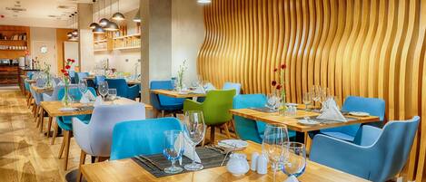 A modern restaurant with wooden floors, blue and green chairs, and wooden walls with a wavy pattern.