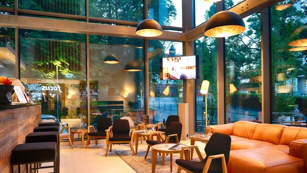 A modern interior with a bar area, seating, and large windows offering a view of the outdoors.