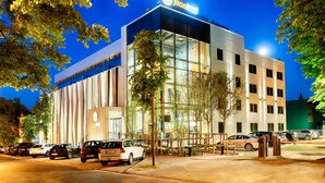 A modern hotel building with a prominent 'Focus Hotel' sign, a parking lot with several cars, and a well-maintained outdoor area with trees.