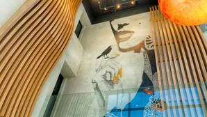 A modern interior with a unique wooden slat design on the walls, a glass railing, and a mural of a bird and a dinosaur.