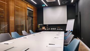 Ein Konferenzraum mit einem langen Tisch, Stühlen, einer Projektionsleinwand und einer Whiteboard-Tafel.