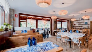 Un restaurant avec des bancs et des tables en bois, de grandes fenêtres et des lampes suspendues.