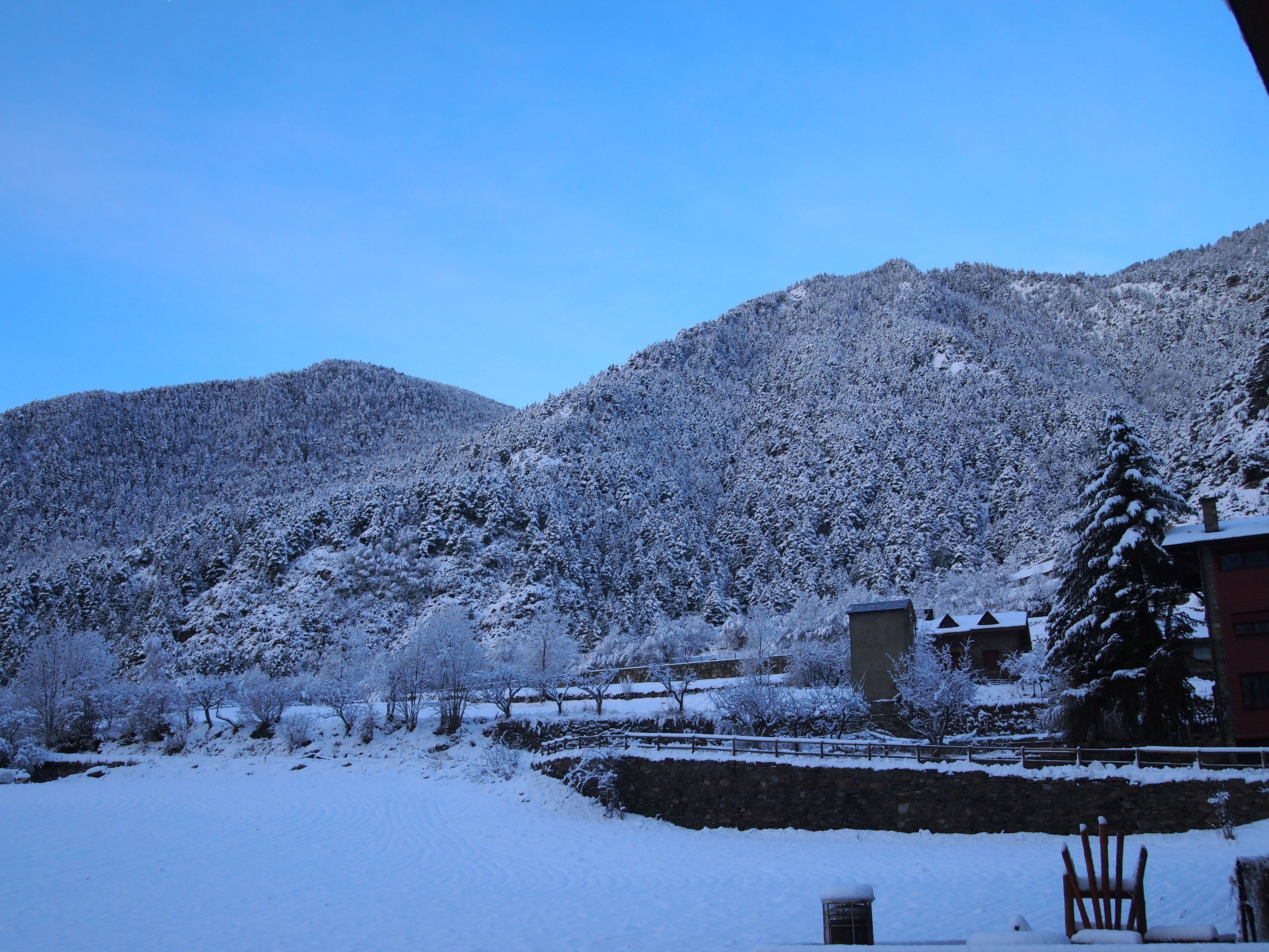 A snow-covered landscape with a stone wall and a wooden chair in the foreground.