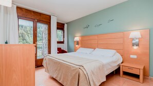 Une chambre avec un grand lit, une tête de lit en bois, des tables de chevet avec des lampes, une vue sur les arbres par la fenêtre et un balcon.