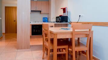 Een compacte keuken met houten kastjes, een magnetron en een kleine eettafel met stoelen.