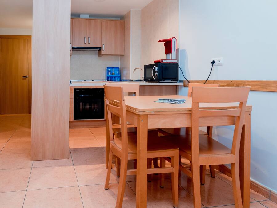 Een compacte keuken met houten kastjes, een magnetron en een kleine eettafel met stoelen.
