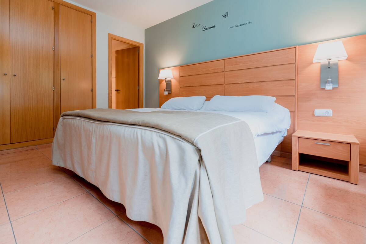 Een slaapkamer met een bed, een houten kledingkast, nachtlampjes en een muur met inspirerende citaten.