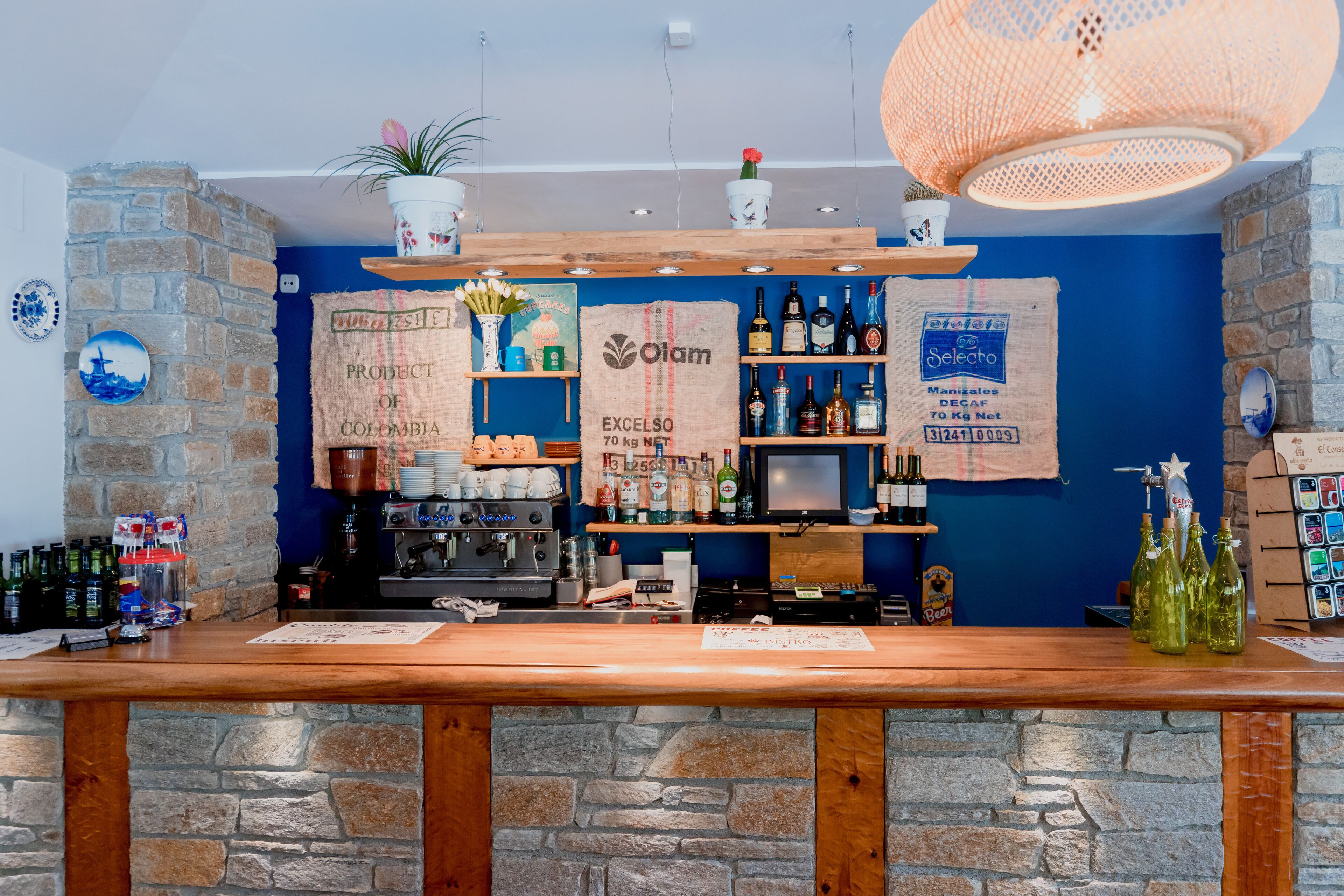Een bar met een stenen muur, een houten toonbank en planken met flessen en een koffieapparaat.