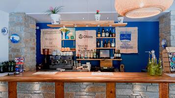 Een bar met een stenen muur, een houten toonbank en planken met flessen en een koffieapparaat.