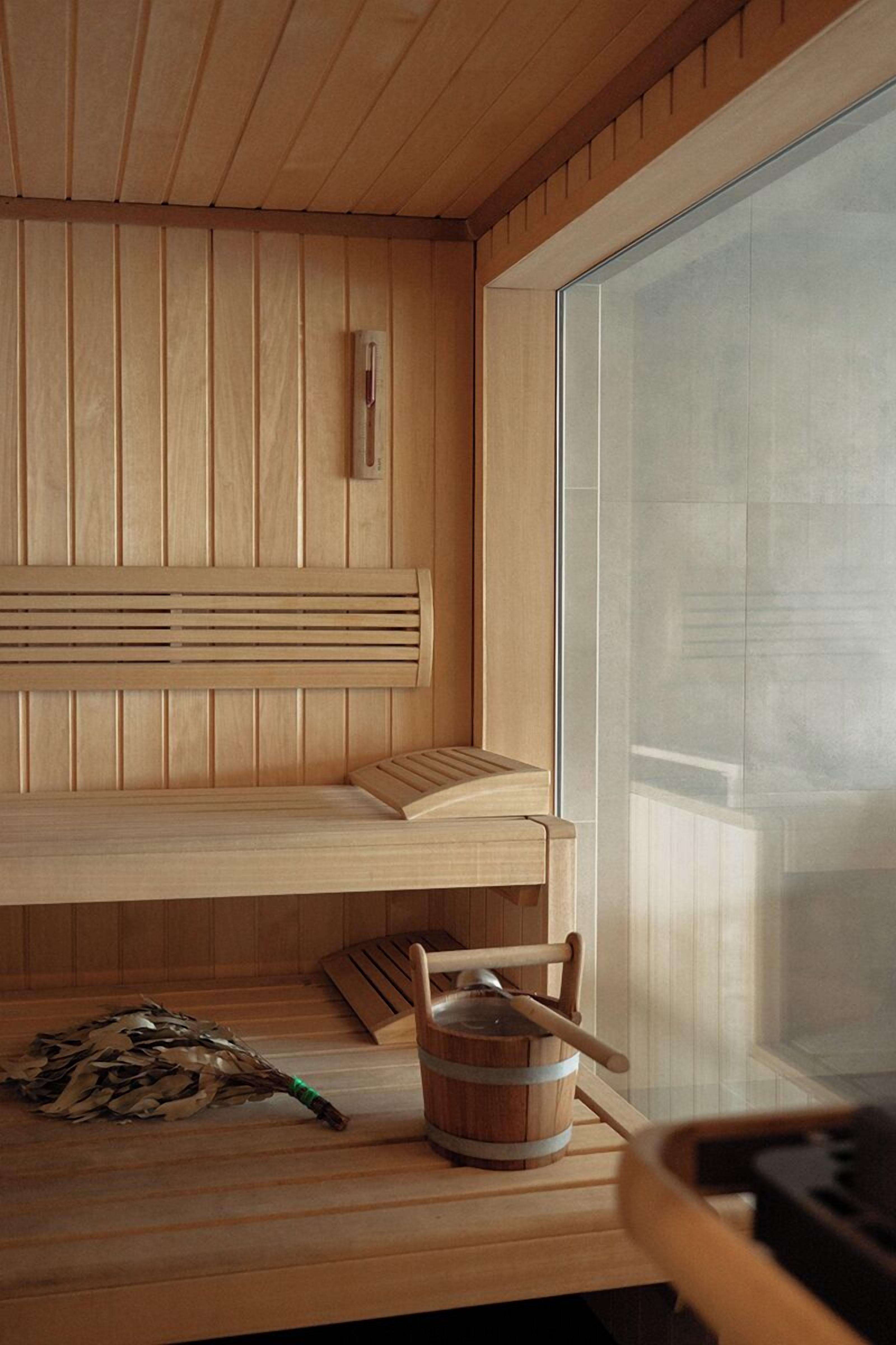 A wooden sauna with a bench, a bucket, and a birch branch.