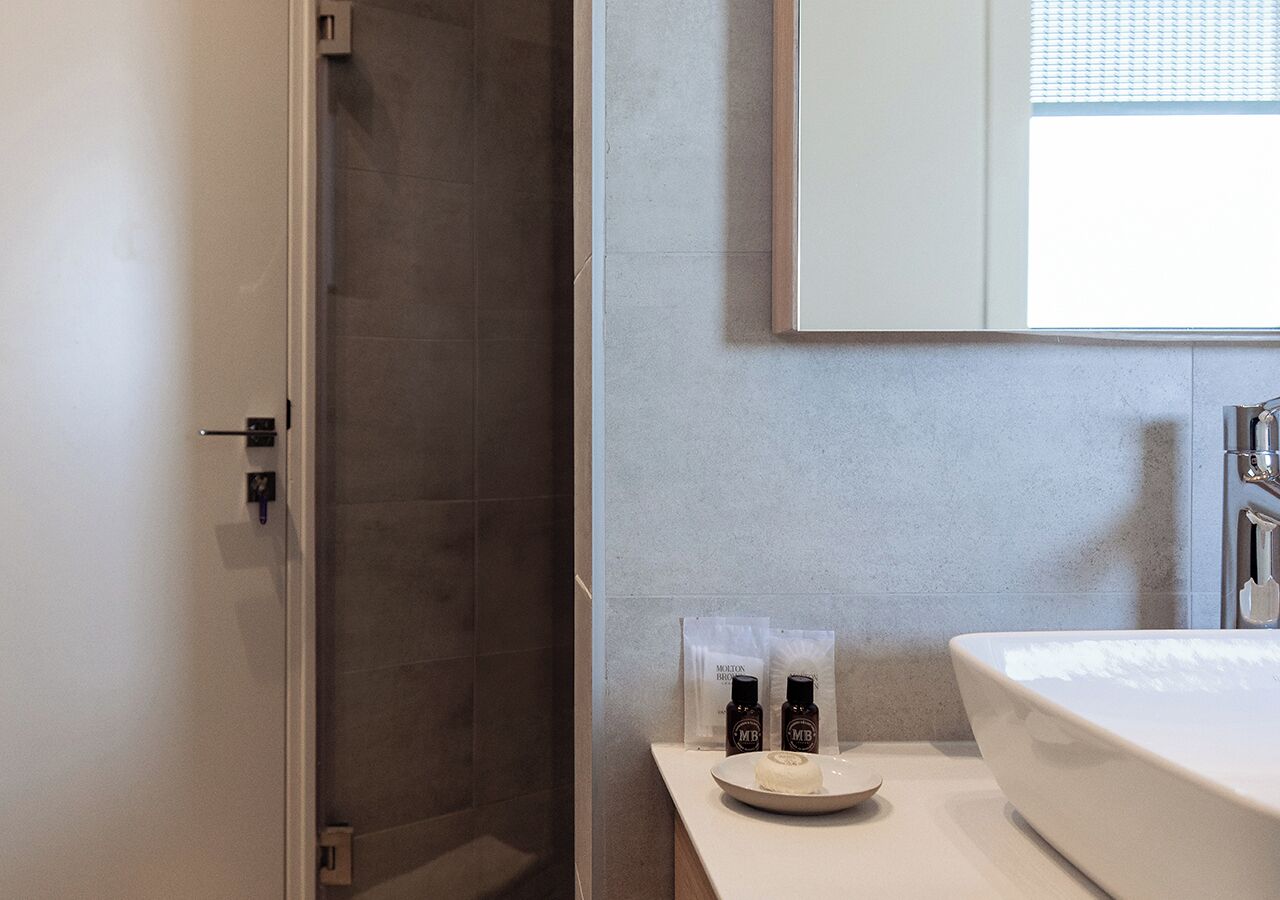 Un baño con ducha, lavamanos y dos botellas sobre el mostrador.