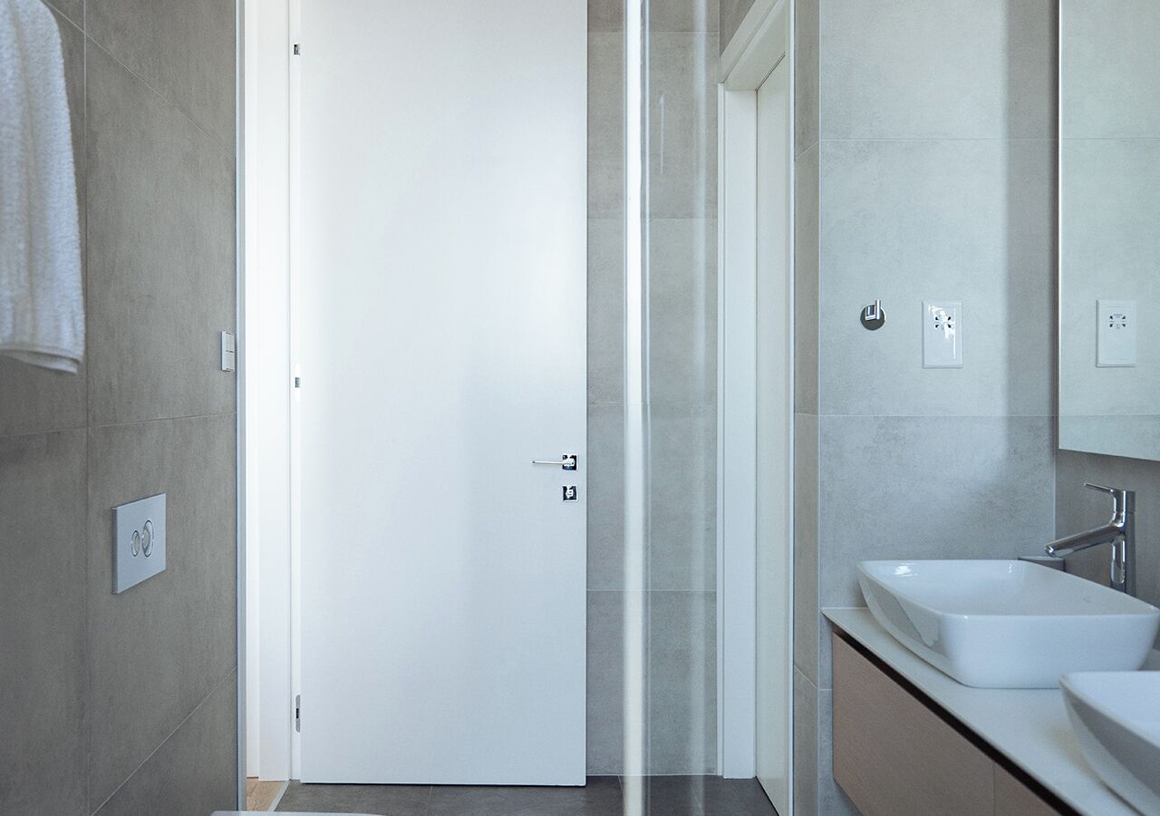 Ein modernes Badezimmer mit einer weißen Tür, einer Duschkabine aus Glas und einem Waschbecken mit Spiegel darüber.