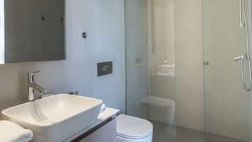 Un baño moderno con un espejo grande, un lavamanos blanco, un inodoro y una zona de ducha con mampara de vidrio.