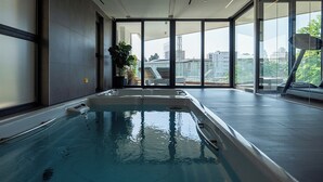 Una piscina interior con paredes de vidrio transparente y vistas a la ciudad, con un diseño moderno.