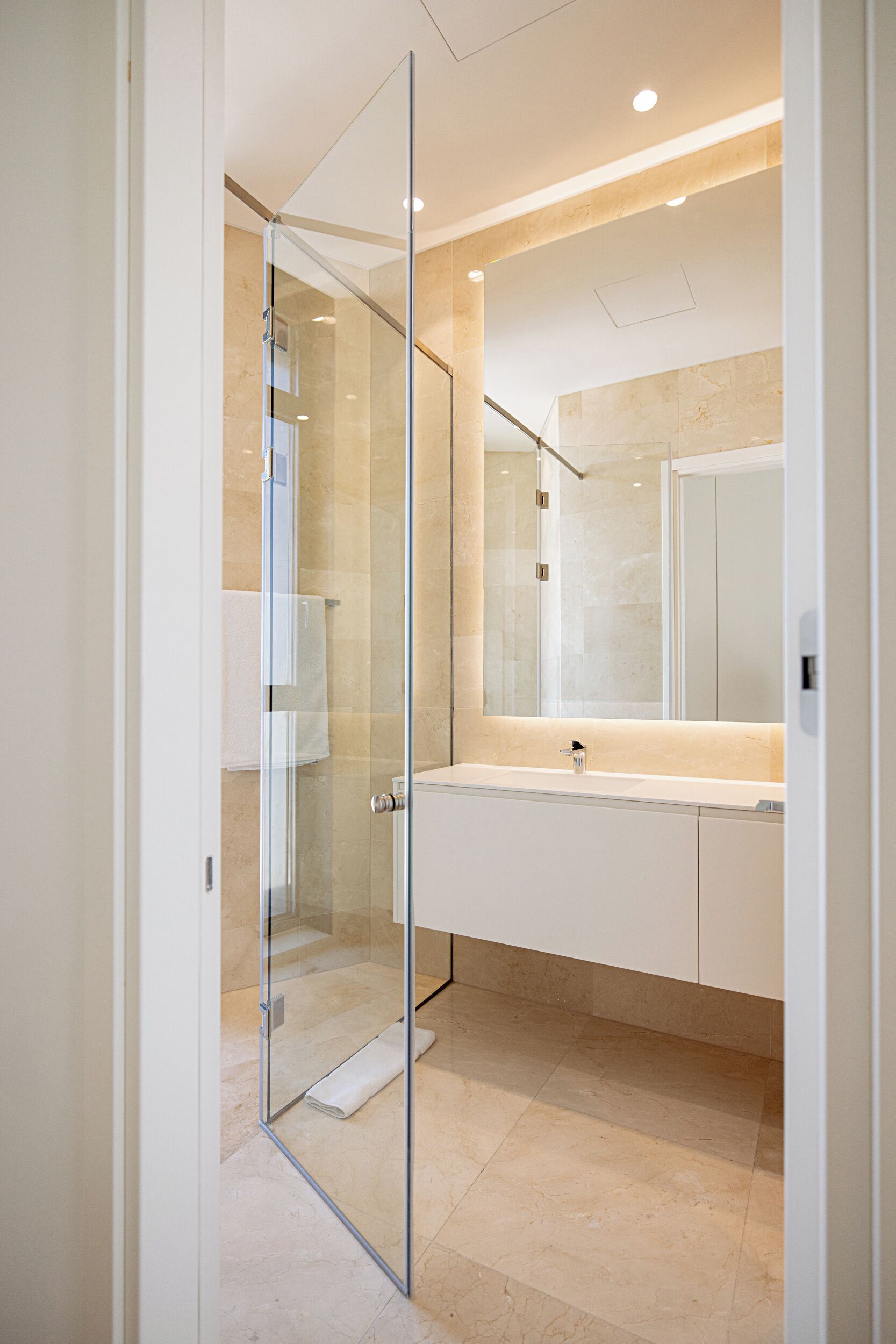 A modern bathroom with a glass shower enclosure, a large mirror, and a white vanity.