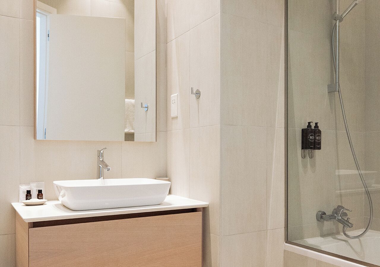 A modern bathroom with a large white sink, a mirror, and a glass-enclosed shower area.