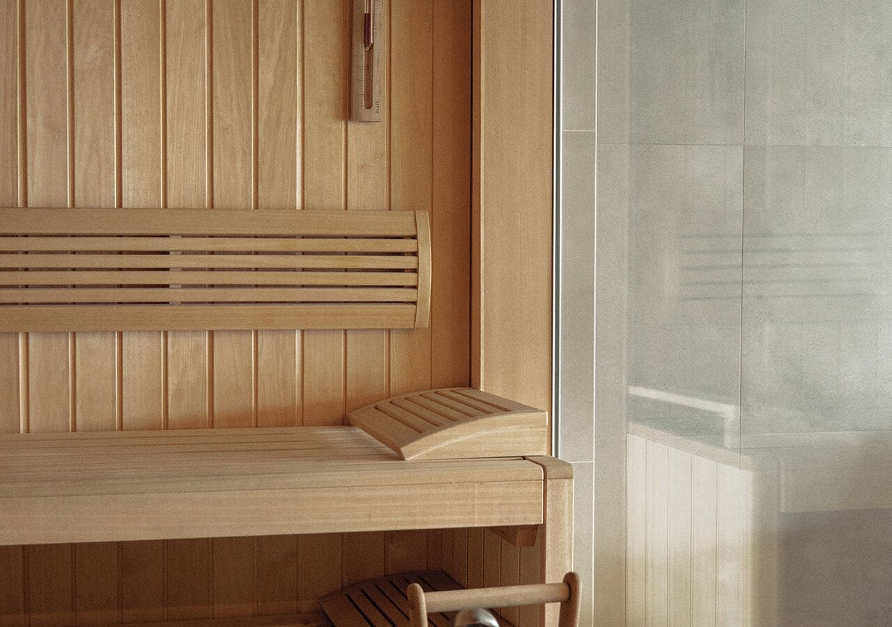 A wooden bench with slatted backrest and seat, positioned against a wall with vertical wooden panels.