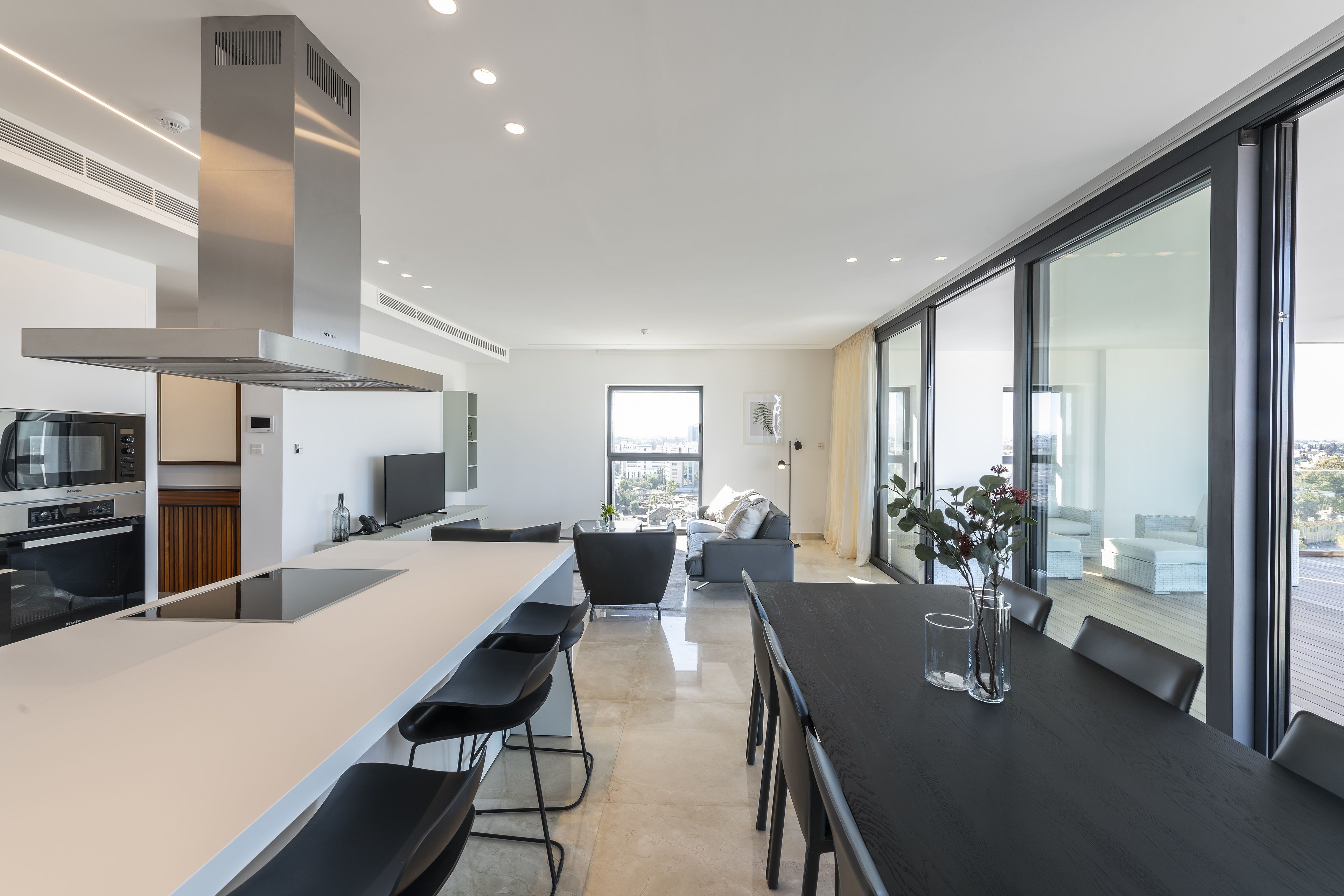 A modern kitchen with a central island, bar stools, and a dining area with a table and chairs.
