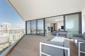 Un balcón moderno con suelo de madera, sofás grises y una mesa blanca.