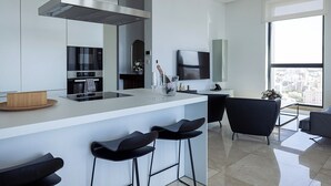 A modern kitchen with a central island, bar stools, a built-in oven, and a large window offering a city view. - Central Park Residence (Nicosia)