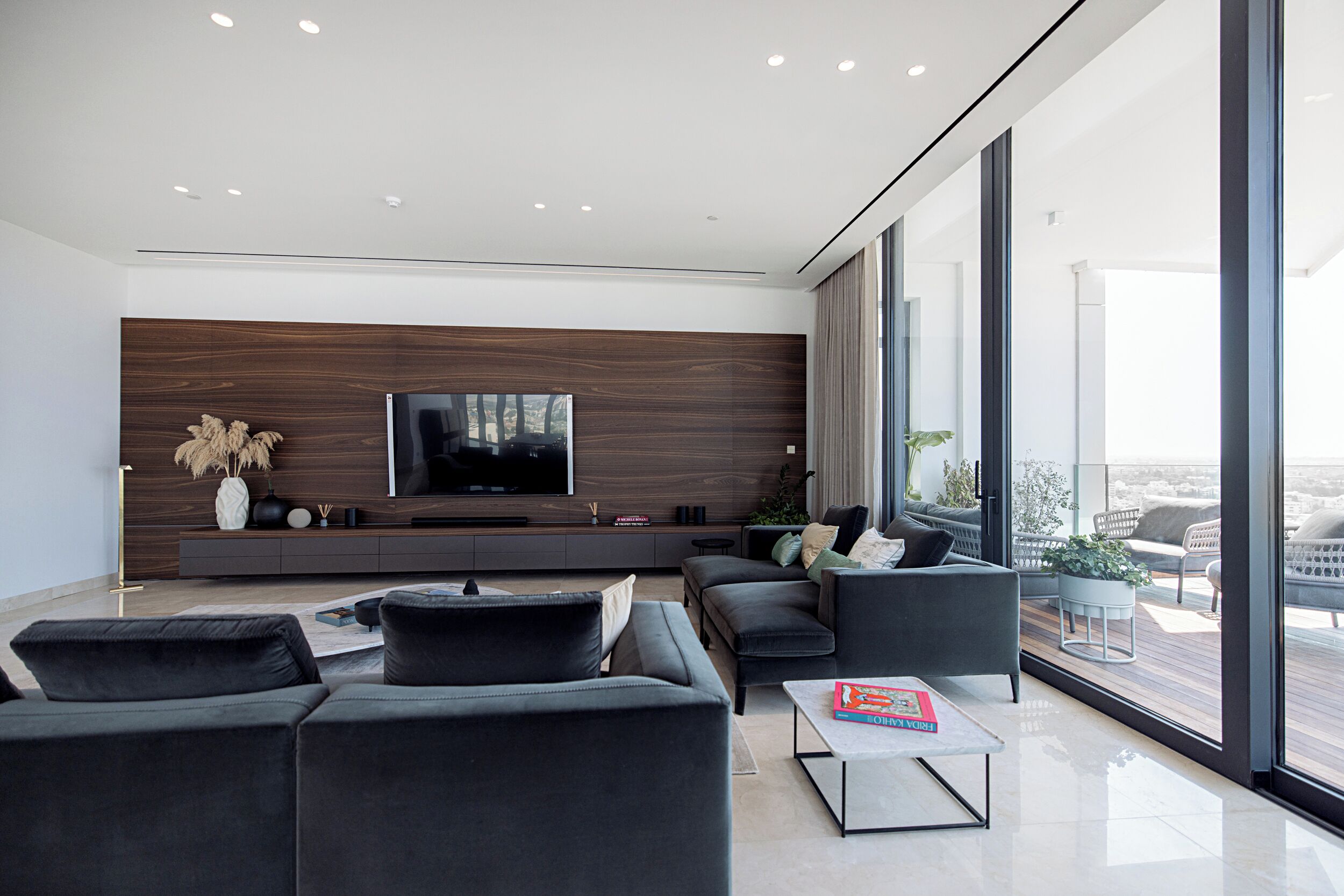 Sala de estar moderna com uma grande TV de tela plana, painéis de madeira escura e vista da cidade através de amplas janelas.