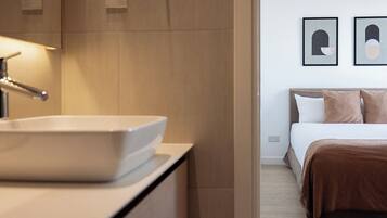 Un baño moderno con un lavabo blanco y una mesita de noche. La habitación tiene una cama con una manta marrón y dos cuadros enmarcados en la pared.