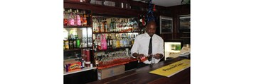 Un bar con estantes repletos de botellas de licores, una zona de bar de día y un cartel que anuncia una selección especial de sidra.