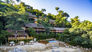 A beachfront resort with multiple thatched-roof buildings, a swimming pool, and a sandy beach.