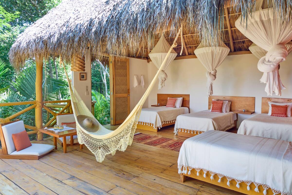 A tropical-style bedroom with a thatched roof, hammocks, and wooden furniture.