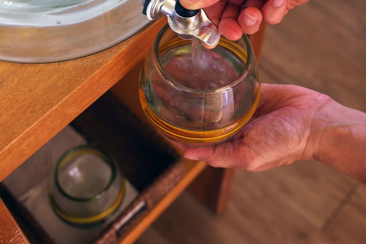 A person filling a glass with water from a large container.