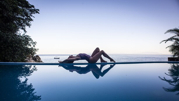 A person lying on a pool deck with a view of the sea and a boat in the background.