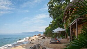 A beach with lounge chairs and a thatched-roof structure.