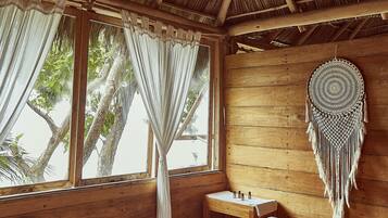 Relax in this serene room with a comfortable bed, ceiling fan, and dreamcatcher, surrounded by natural light and a cozy atmosphere.