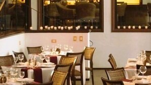 Un restaurante con varias mesas preparadas para comer, sillas de mimbre e iluminación colgante.
