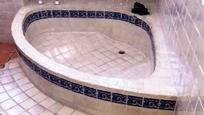 Un jacuzzi con borde de azulejos azules y blancos, integrado en una esquina de una habitación con suelo de baldosas de terracota.