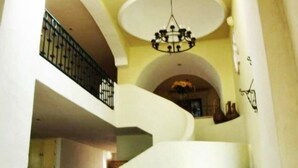 Un interior espacioso con una escalera curva, un candelabro y vistas a un comedor.