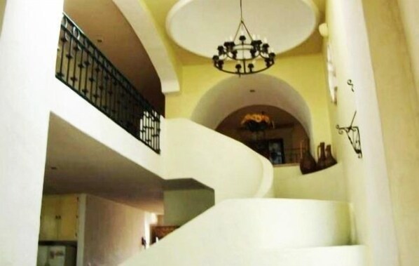 A spacious interior with a curved staircase, a chandelier, and a view of a dining area.