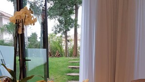 A modern dining area with a glass table, white chairs, and a view of a garden. - Engy Estoril - Luxury Villas (Cascais)