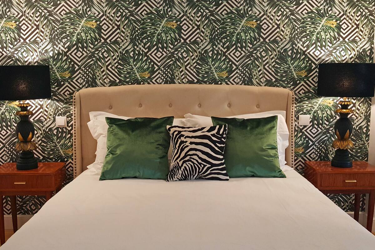 Ein Bett mit beigem Kopfteil, zwei Nachttische mit Lampen und rahmigem Wandpapier.