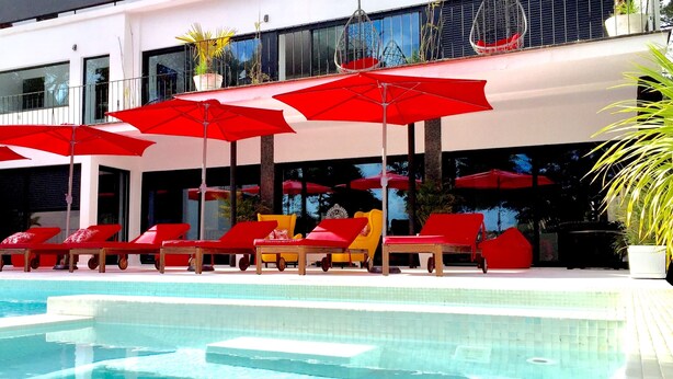 A pool area with red umbrellas, lounge chairs, and a clear pool. - Engy Estoril - Luxury Villas (Cascais)