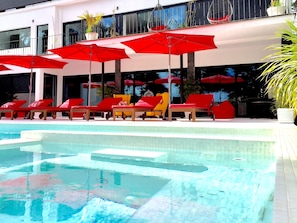 A pool area with red umbrellas, lounge chairs, and a clear pool. - Engy Estoril - Luxury Villas (Cascais)